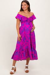 woman wearing a bright pink off-shoulder maternity dress with floral pattern and a knotted front, holding her baby bump