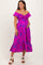 woman wearing a bright pink off-shoulder maternity dress with floral pattern and a knotted front, holding her baby bump