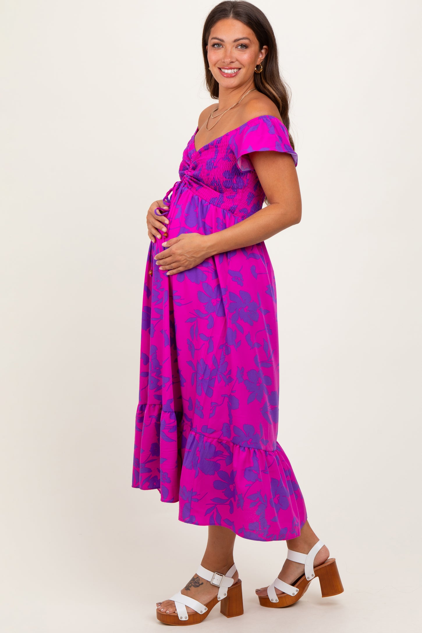 woman wearing a vibrant pink floral off-the-shoulder maternity dress and holding her baby bump