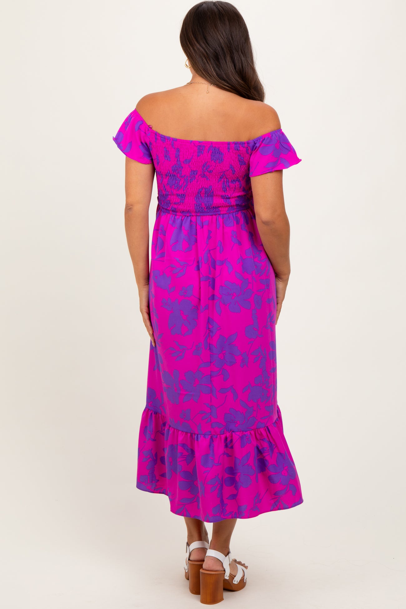 woman wearing a vibrant pink off-the-shoulder maternity dress with floral design and ruffle hem, showing her baby bump.