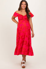 woman wearing a bright pink floral off-shoulder maternity dress with ruching and a ruffled hem, displaying her baby bump