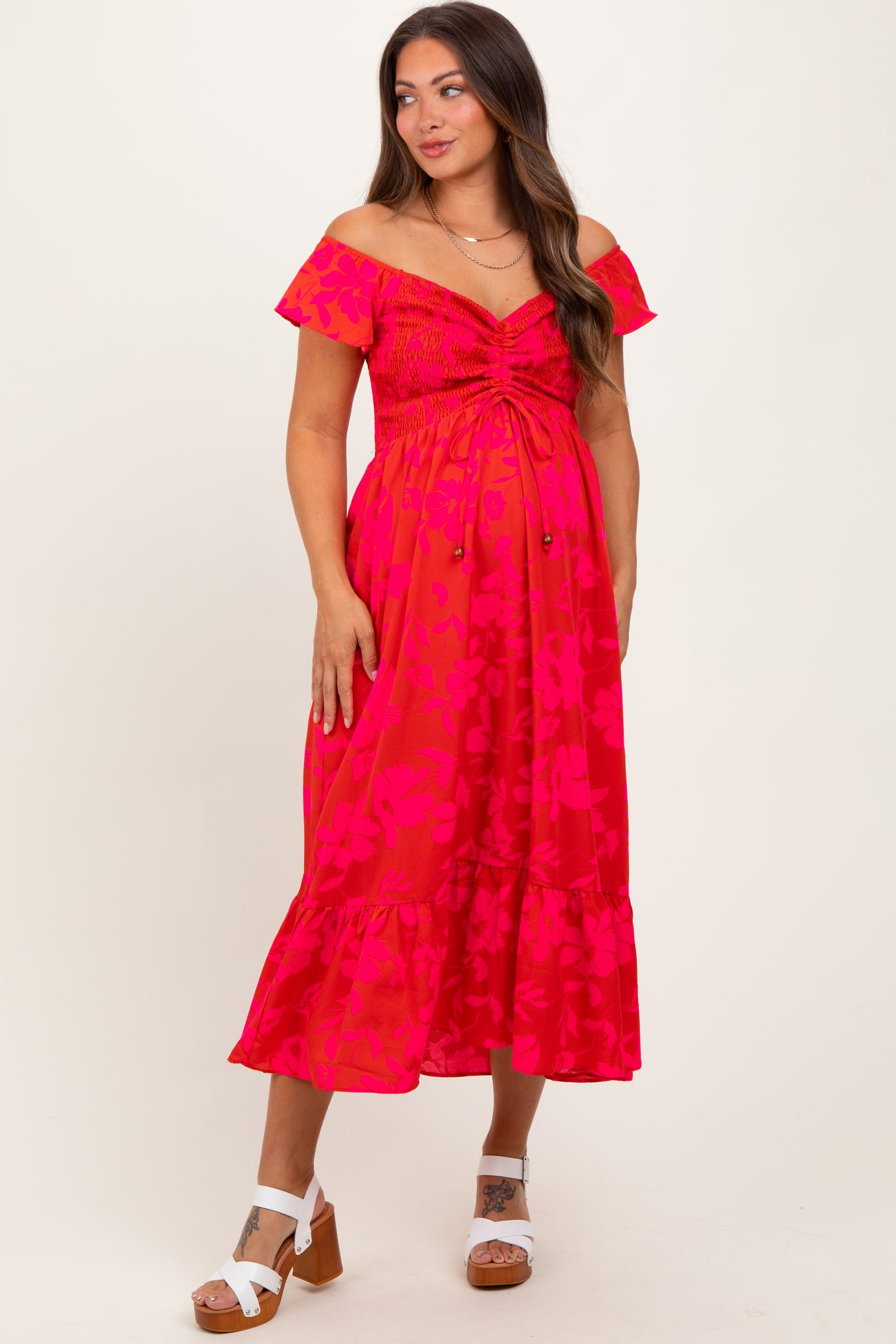 woman wearing a hot pink floral off-shoulder maternity dress with a smocked bodice and ruffle hem, showing her baby bump