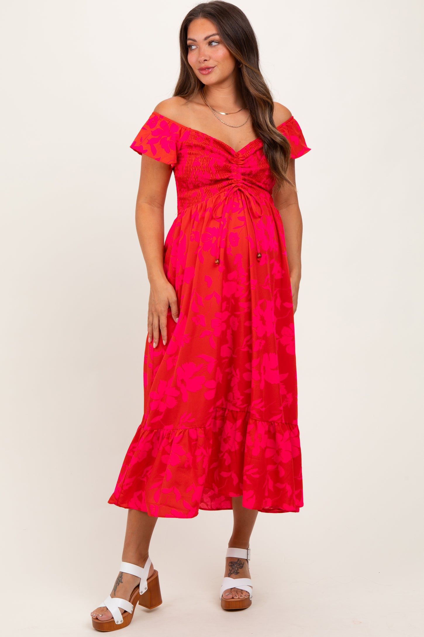 woman wearing a hot pink floral off-shoulder maternity dress with a smocked bodice and ruffle hem, showing her baby bump