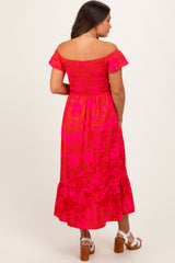 woman wearing a pink floral off-shoulder maternity dress with a smocked bodice and ruffle hem