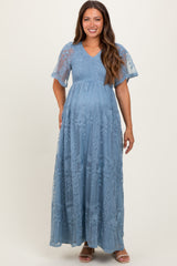 woman wearing a blue maternity maxi dress with flutter sleeves and floral embroidery, showcasing her baby bump