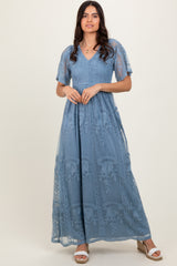 woman wearing a blue maxi dress with embroidered floral details and short flutter sleeves