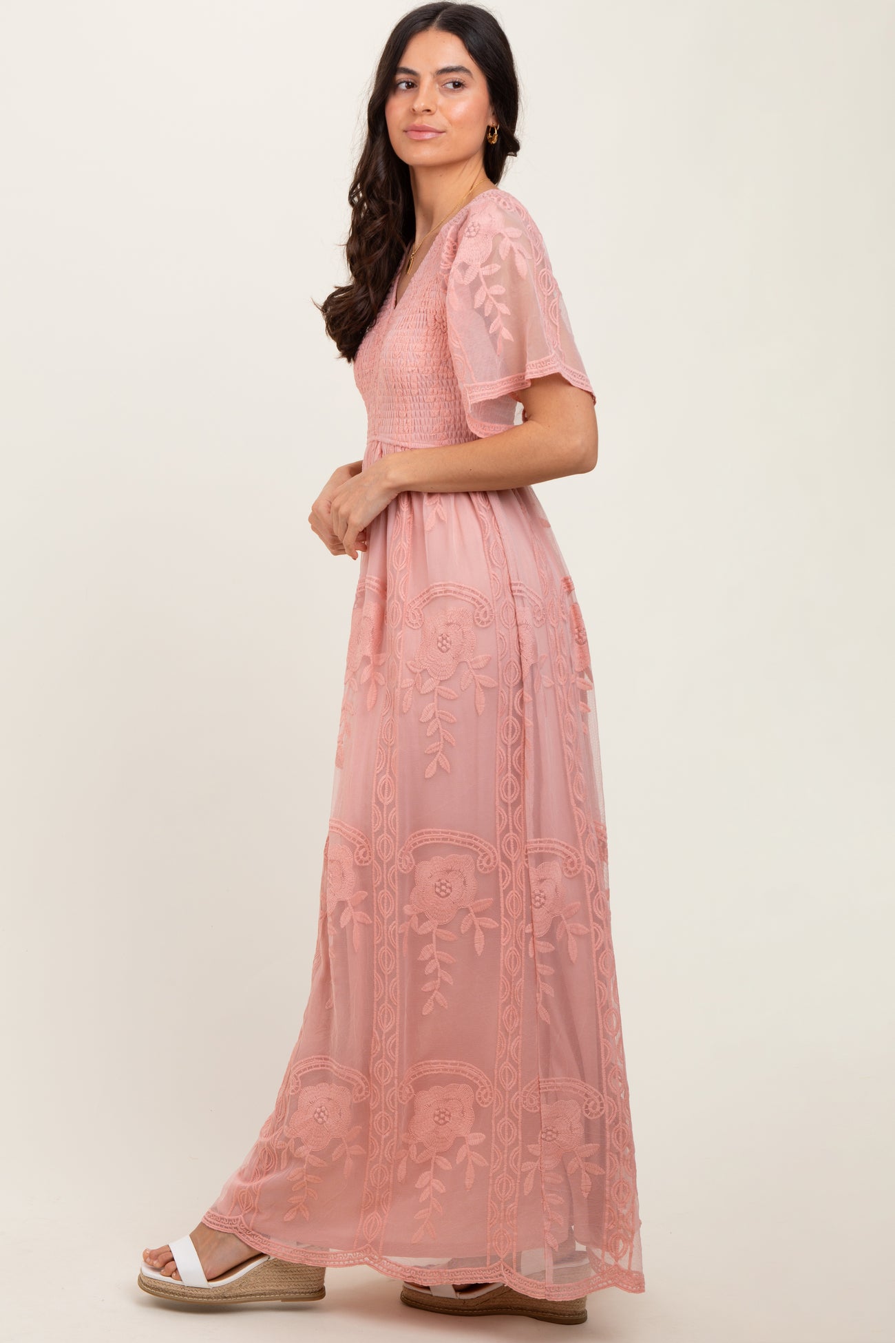 woman wearing a dusty pink maxi dress with floral embroidery and short sleeves, posing sideways against a neutral background