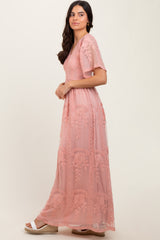 woman wearing a dusty pink maxi dress with floral embroidery and short sleeves, posing sideways against a neutral background