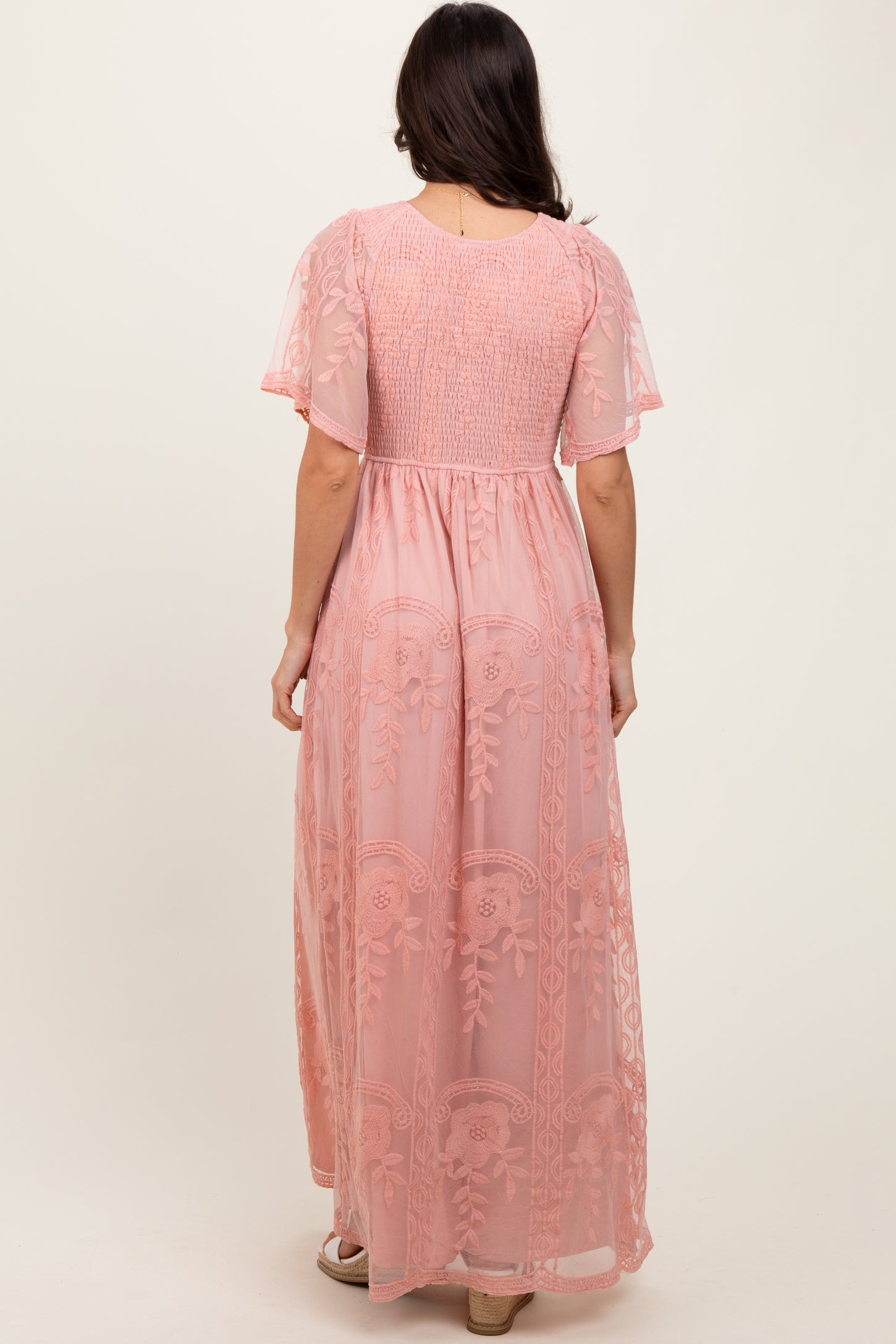 woman wearing a pink maxi dress with gathered sleeves and floral embroidery, photographed from the back