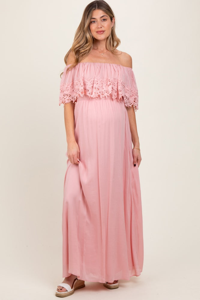woman wearing a light pink off-the-shoulder maternity maxi dress with floral lace details and a visible baby bump