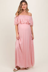 woman wearing a light pink off-the-shoulder maternity maxi dress with floral lace details and a visible baby bump