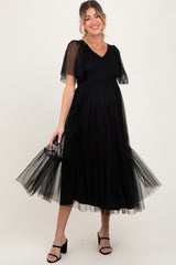 woman wearing a black maternity dress with short puff sleeves and a tulle ruffled hem, showing her baby bump
