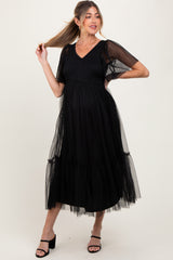 woman wearing a black maternity dress with puff sleeves and tulle detailing, showing her baby bump