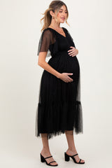 woman wearing a black maternity dress with tulle sleeves and a tiered skirt, cradling her baby bump