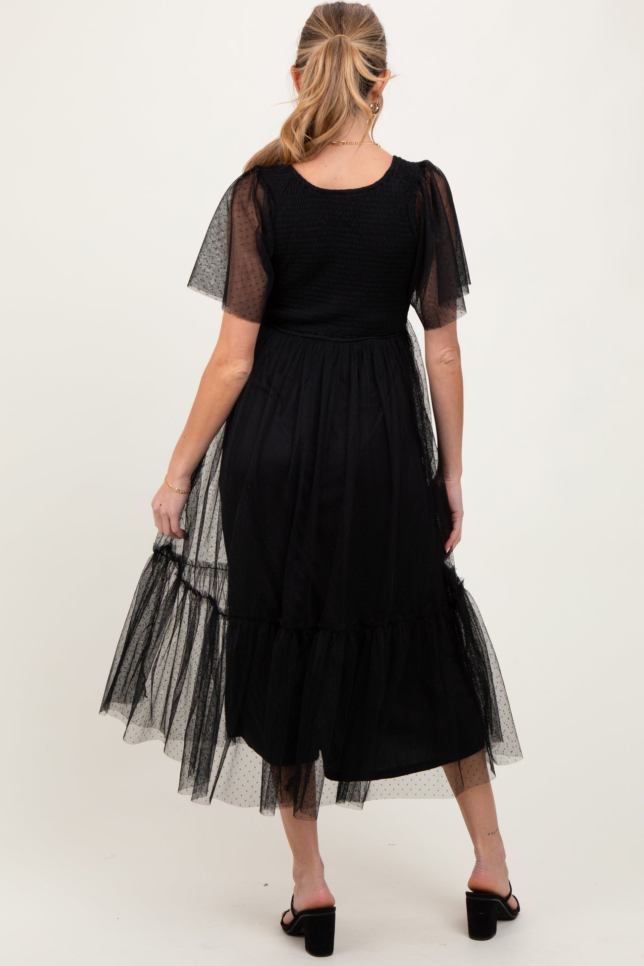 woman wearing a black maternity dress with short sheer puff sleeves and a tiered tulle hem, showing her baby bump