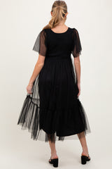 woman wearing a black maternity dress with short sheer puff sleeves and a tiered tulle hem, showing her baby bump