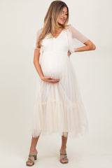 woman wearing a cream maternity dress with short puff sleeves and tiered tulle skirt, cradling her baby bump