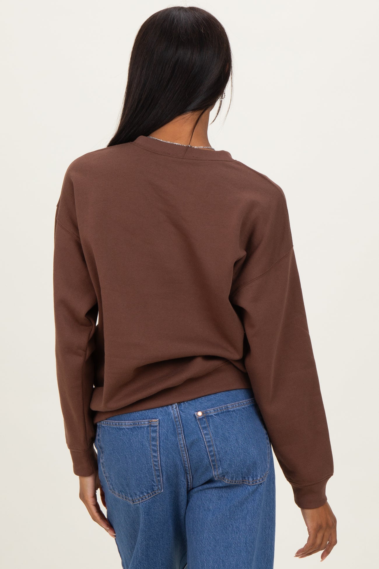 woman wearing a brown oversized sweatshirt with a relaxed fit and blue high-waisted jeans, viewed from the back