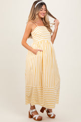 woman wearing a yellow and white striped maternity maxi dress with pockets, smiling and playing with her hair