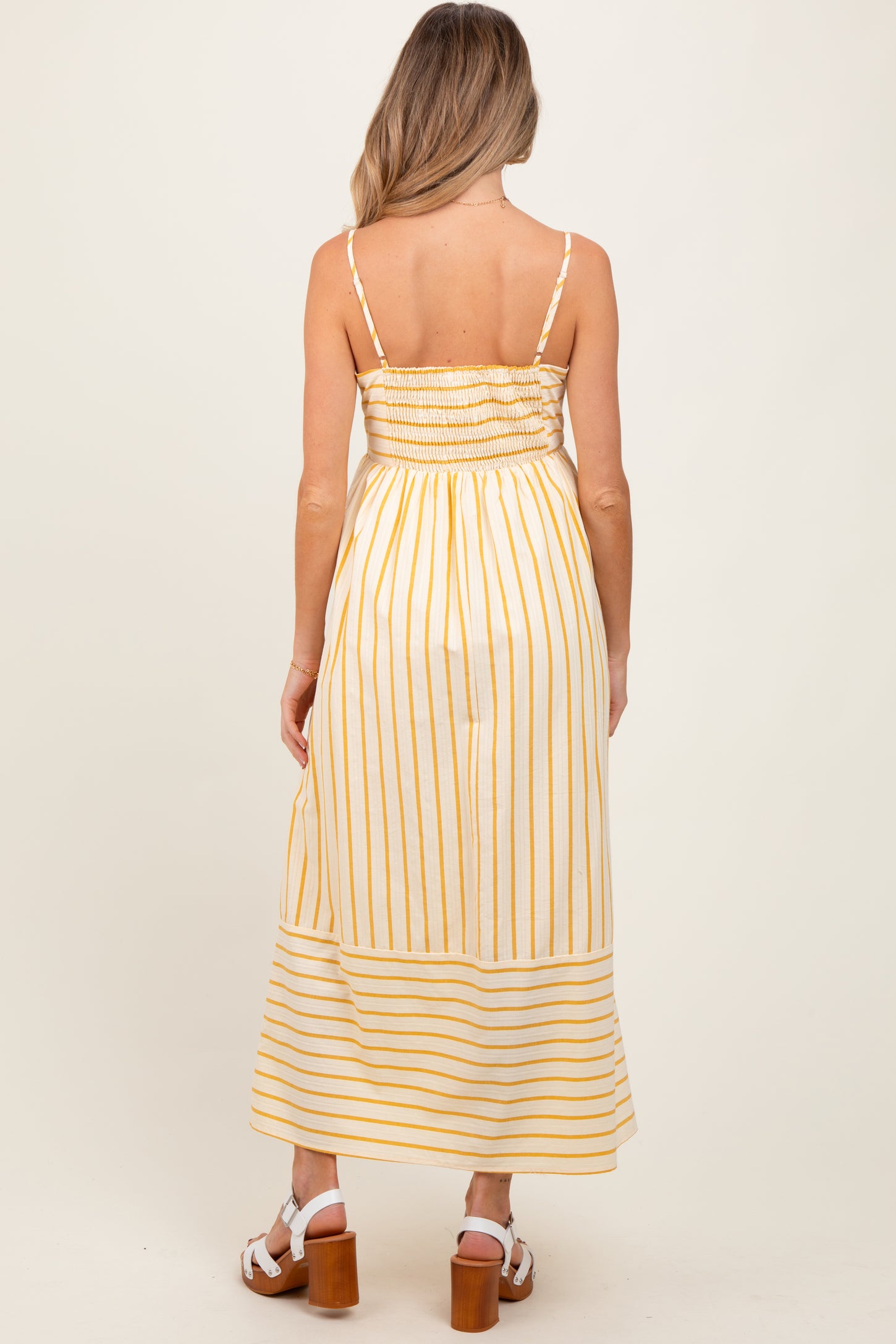 woman wearing a yellow and white striped maternity maxi dress with a smocked bodice and adjustable straps viewed from the back