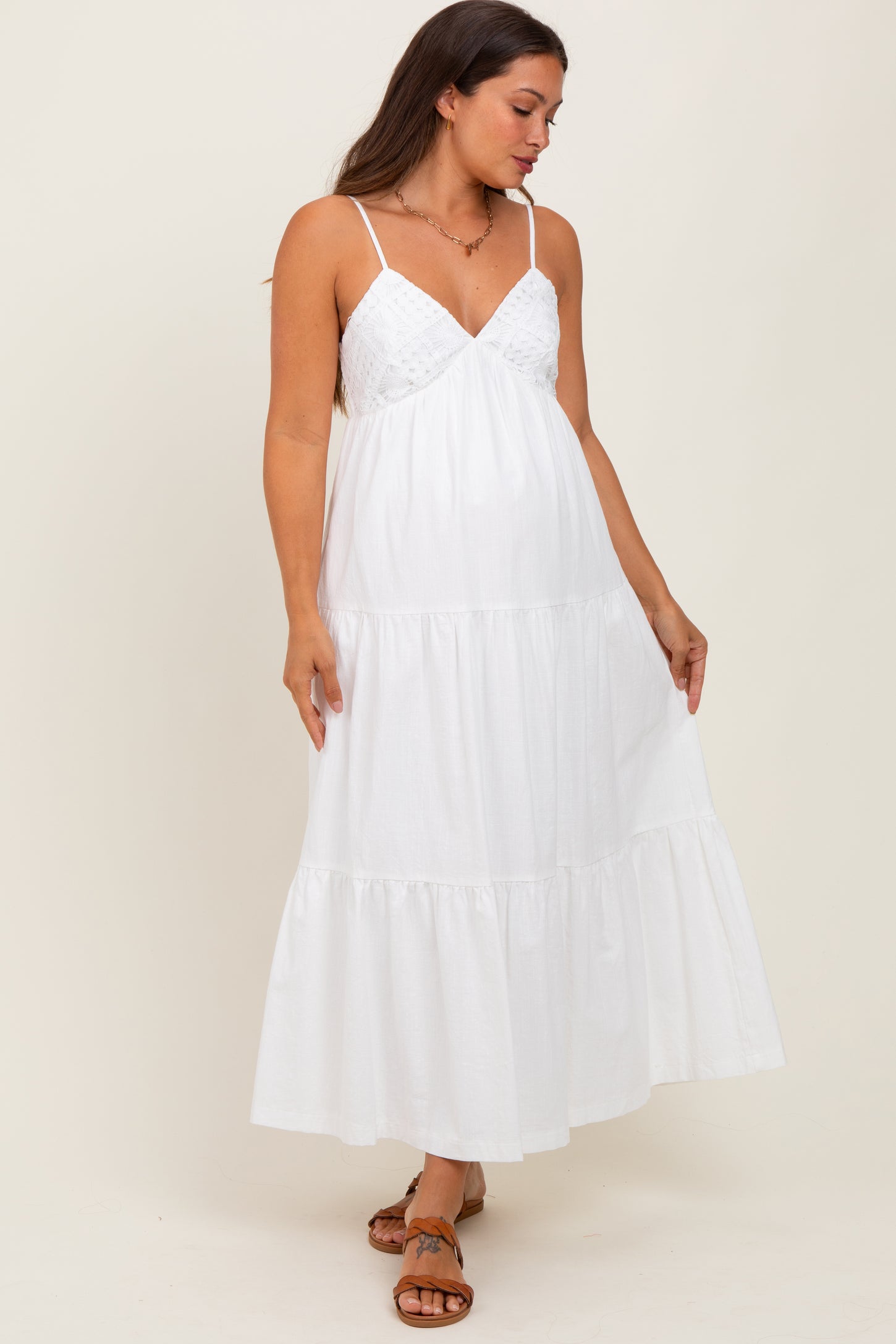 woman wearing a white maternity maxi dress with adjustable straps and tiered ruffles, showcasing a baby bump
