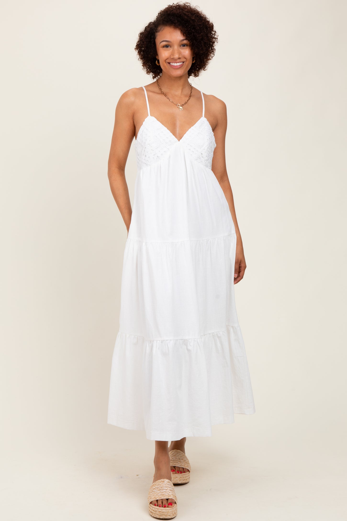 woman wearing a white maxi dress with lace detail and a tiered skirt, standing on a neutral background