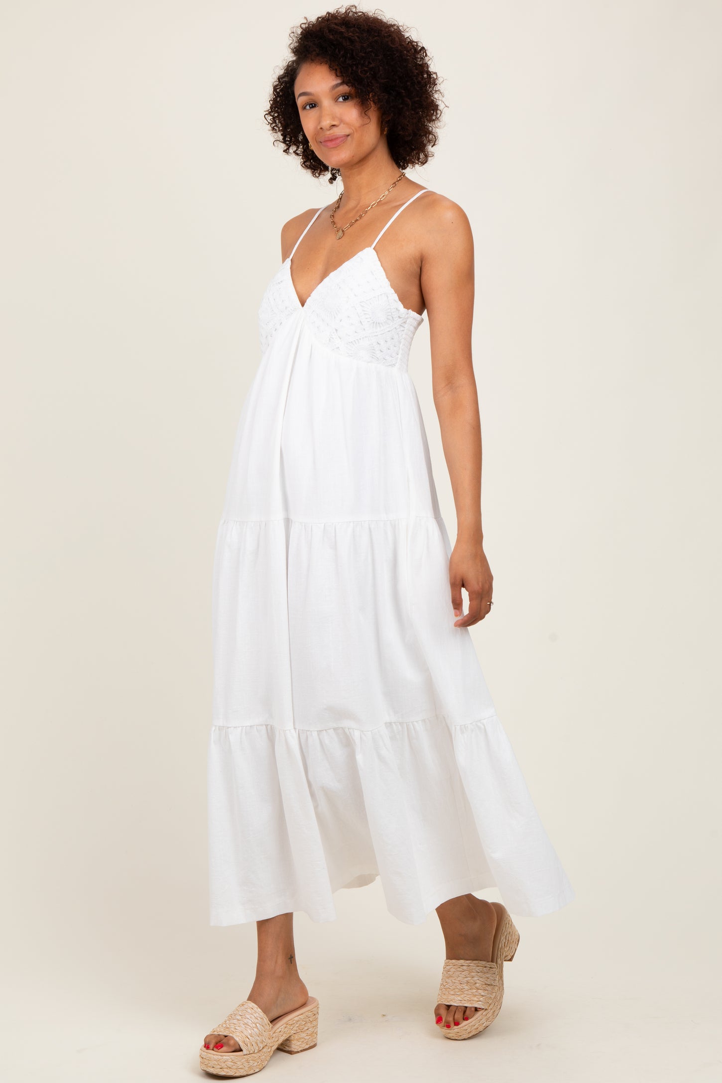woman wearing a white tiered maxi dress with a lace bodice and spaghetti straps, standing in a neutral background