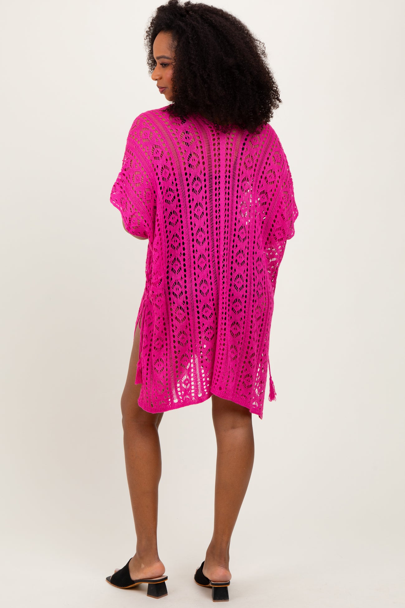 woman wearing a bright pink crochet beach cover-up with a loose fit and side slits shown from the back