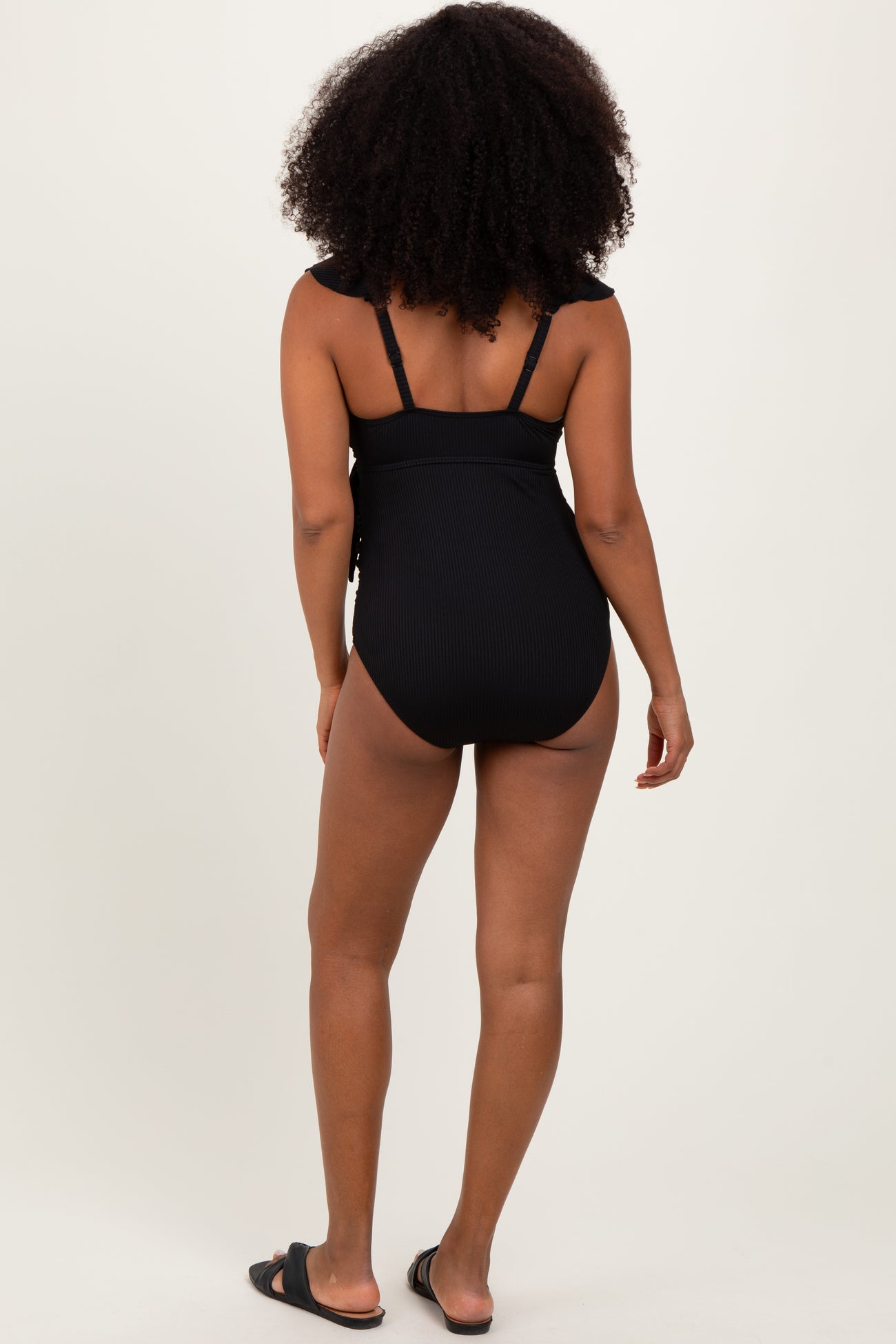 woman wearing a black ribbed one-piece swimsuit with adjustable straps, viewed from the back