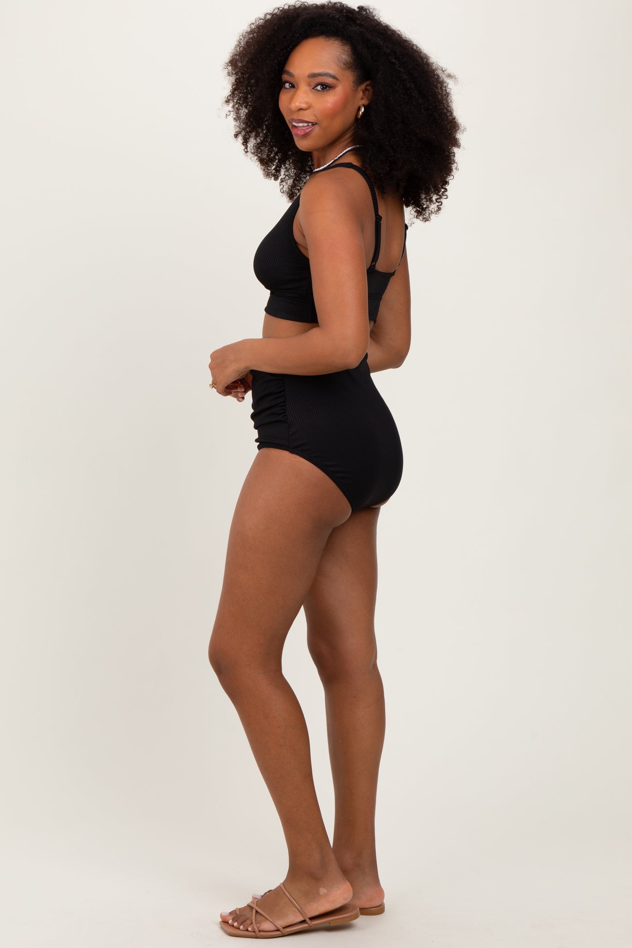 woman wearing a black two-piece bikini with a crop top and high-waisted bottoms, styled with tan sandals