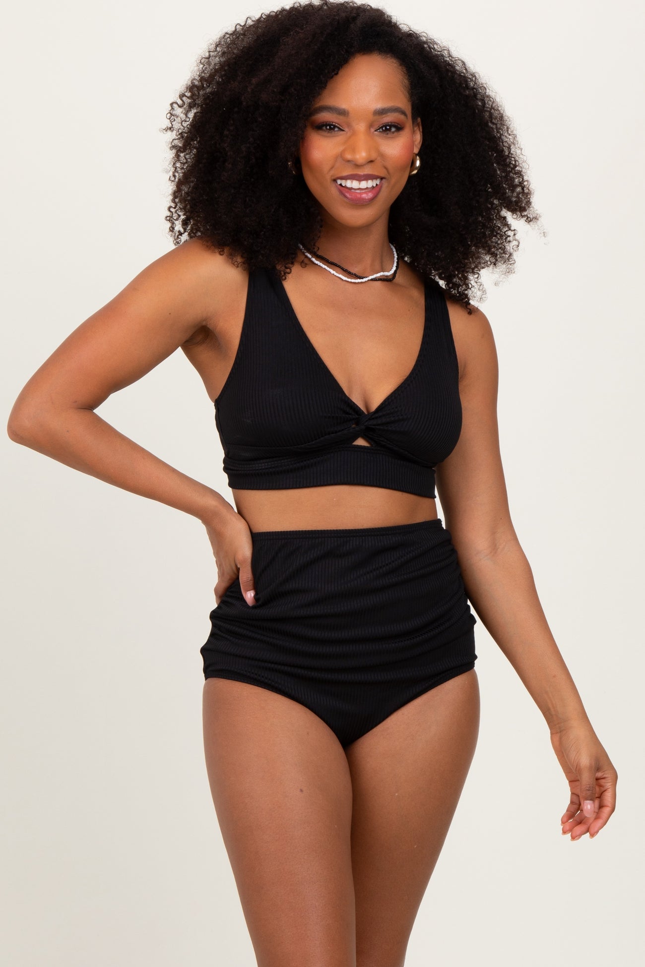 woman wearing a black ribbed bikini top with knot detail and high-waisted bottom, smiling at the camera