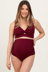 woman wearing a burgundy maternity bikini with a twist front top and high-waisted bottom, baby bump visible