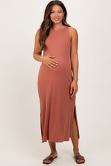 woman wearing a rust-colored sleeveless maternity maxi dress with side slits, gently cradling her baby bump
