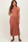 woman wearing a rust-colored sleeveless maternity maxi dress with side slits, gently cradling her baby bump