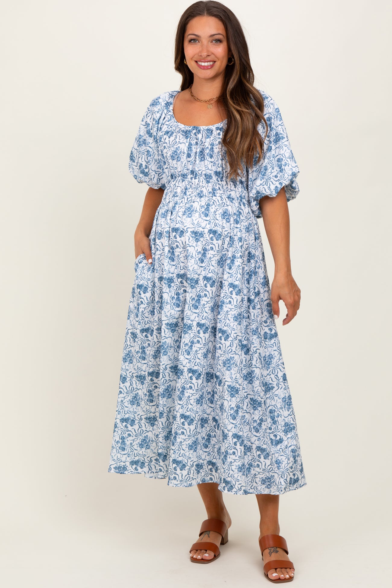 woman wearing a blue and white floral print maternity dress with puff sleeves and pockets, showing her baby bump