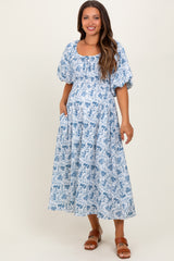 woman wearing a blue and white floral print maternity dress with puff sleeves and pockets, showing her baby bump