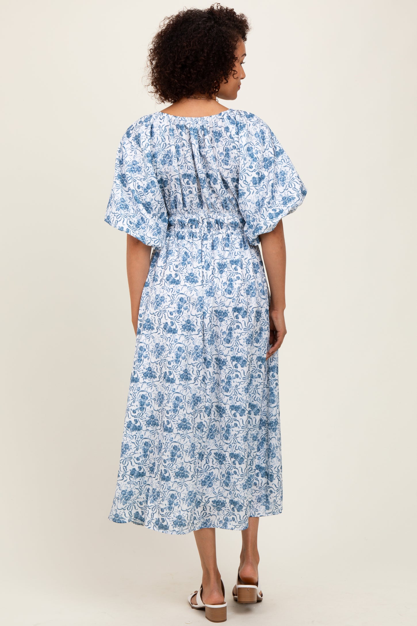 woman wearing a blue and white floral maxi dress with short flutter sleeves and a smocked bodice, viewed from the back