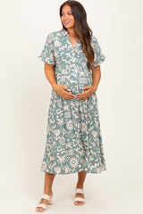 woman wearing a patterned green maternity dress with a tie waist and holding her baby bump