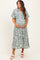 woman wearing a patterned green maternity dress with a tie waist and holding her baby bump