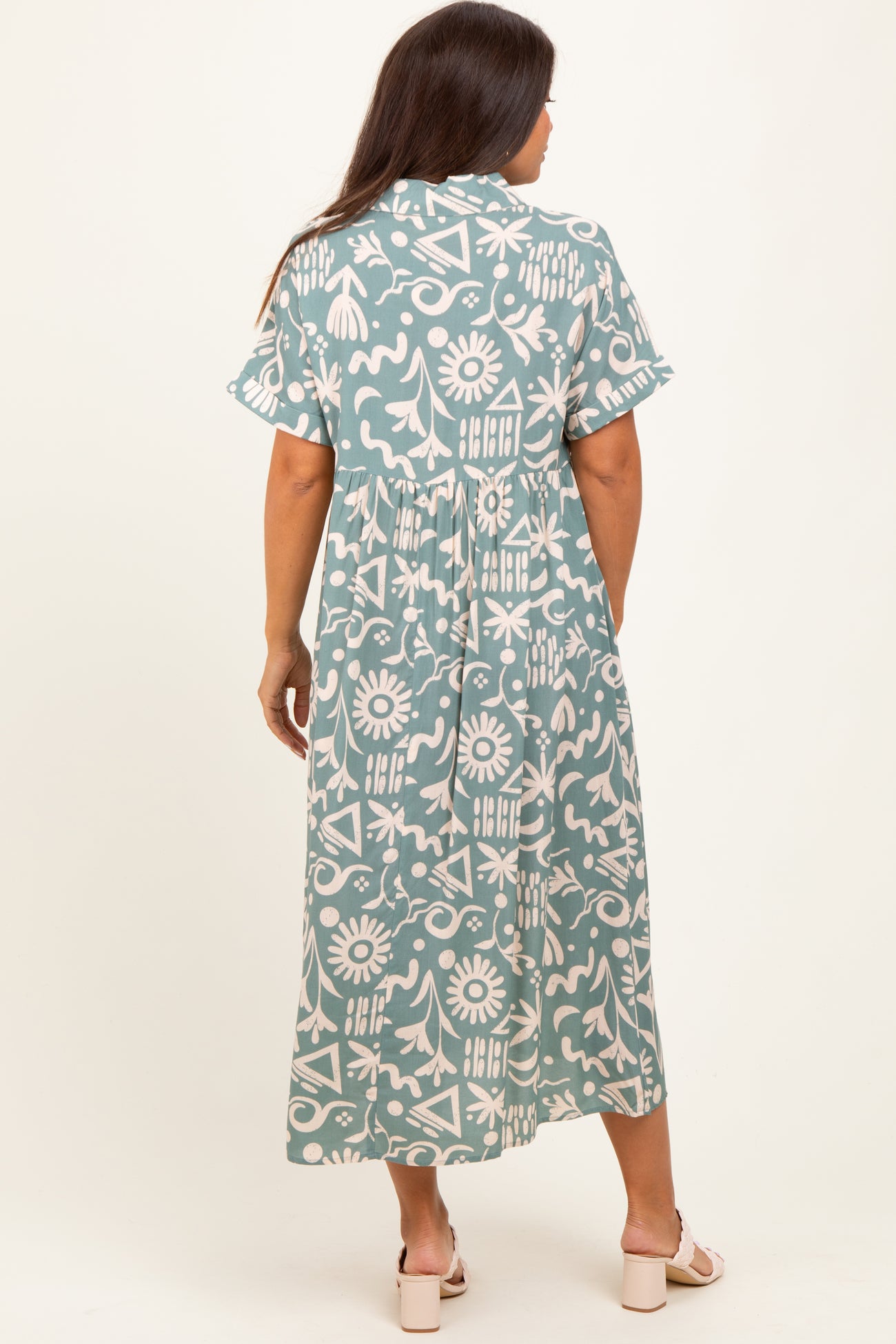 woman wearing a green and white patterned maternity maxi dress, with short sleeves and a relaxed fit, standing with her back to the camera
