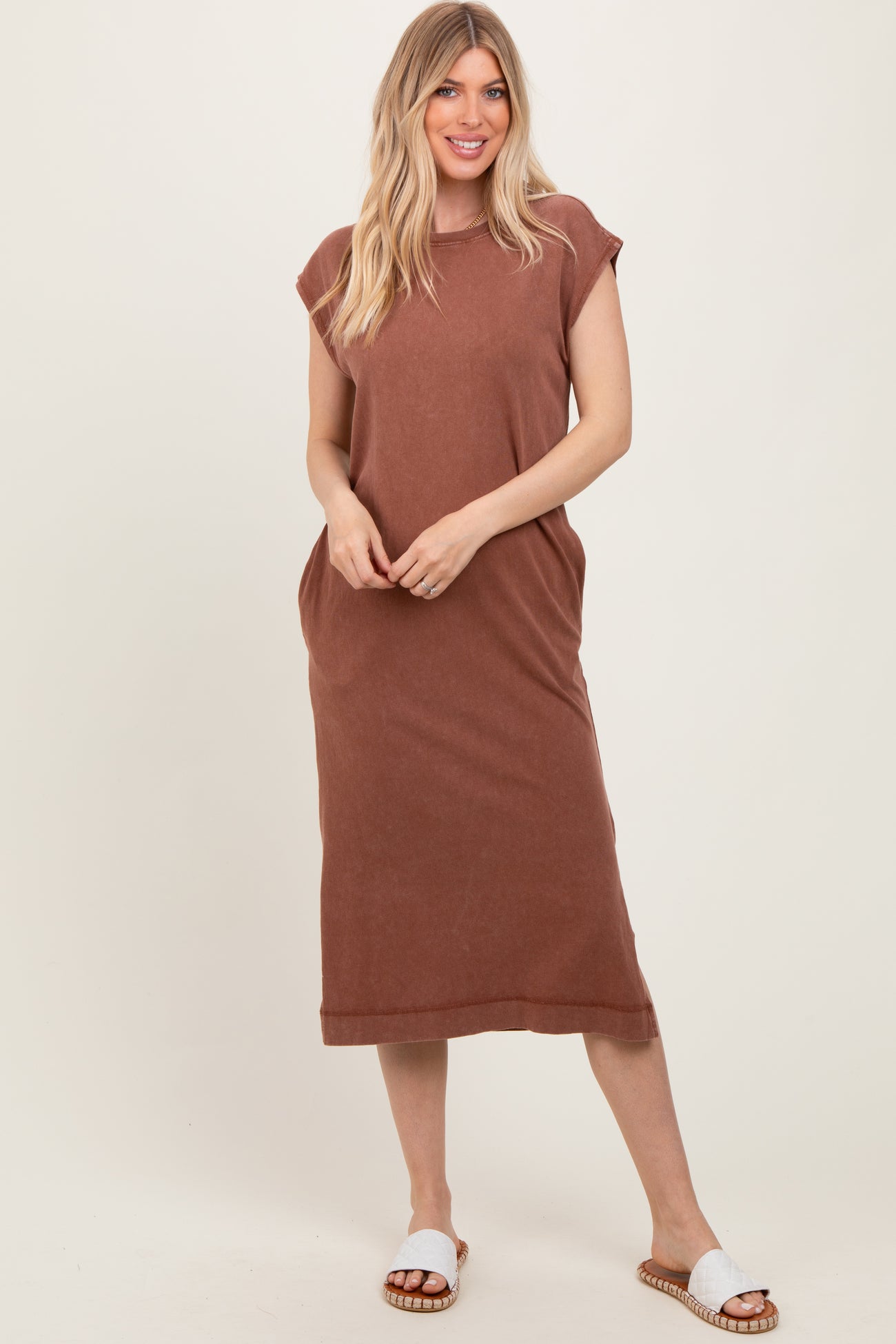 woman wearing a brown sleeveless maxi dress with side pockets and white slide sandals