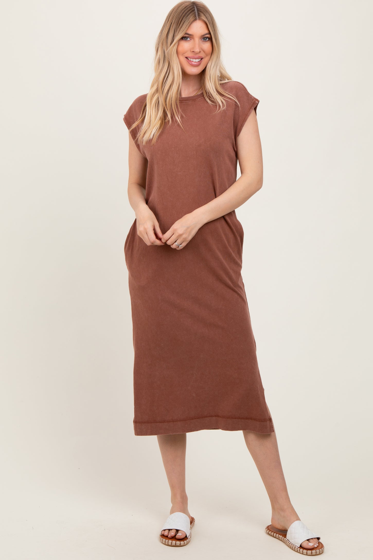 woman wearing a brown sleeveless maxi dress with side pockets and white slide sandals