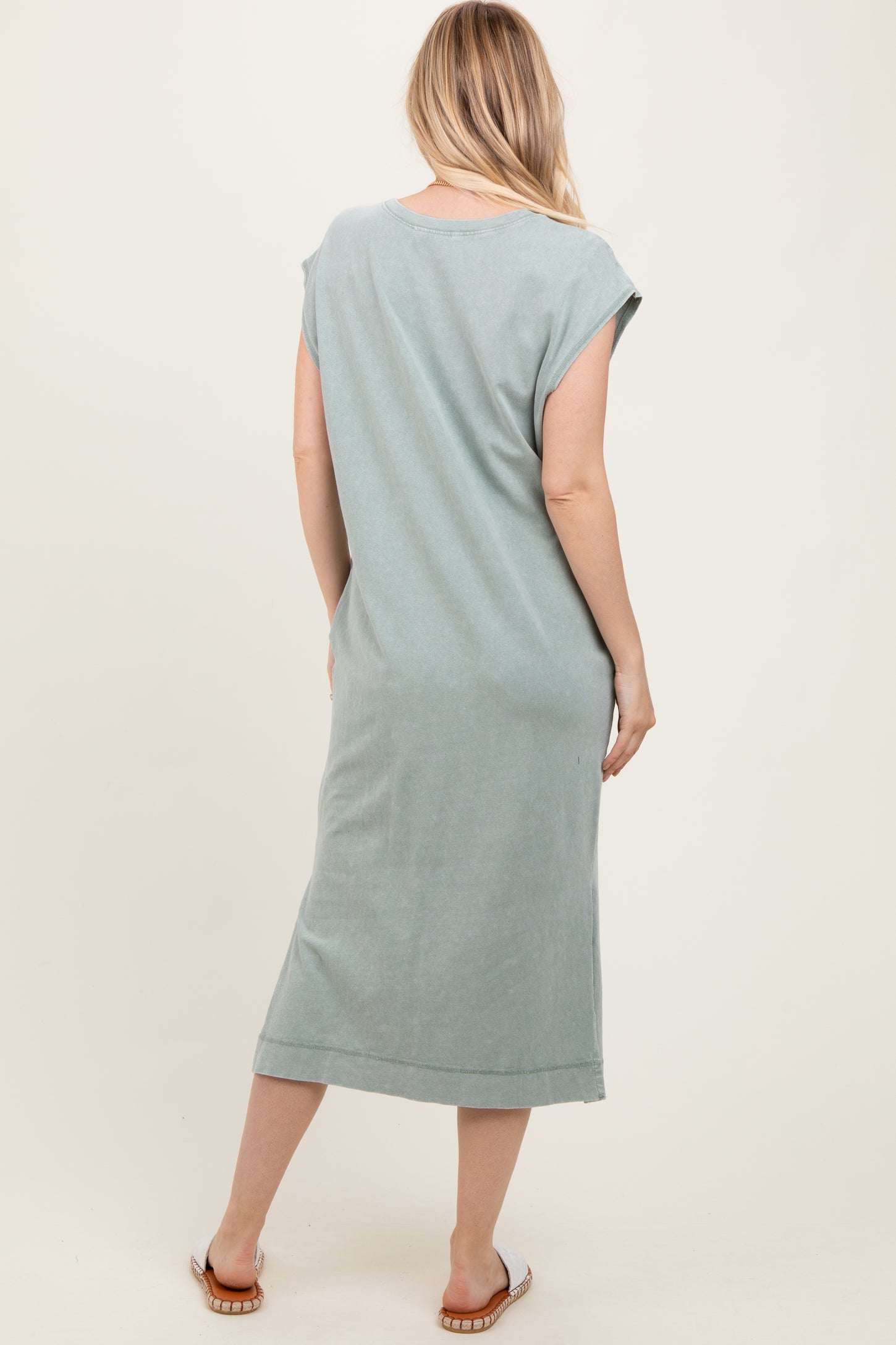 woman wearing a sage green short sleeve midi dress, showing the back view, with a relaxed fit and side slits