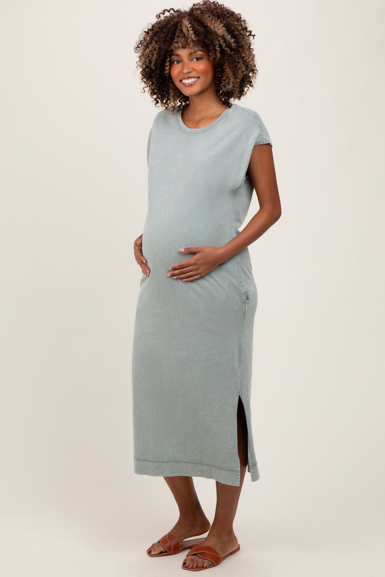 woman wearing a light green maternity maxi dress with side slits and holding her baby bump