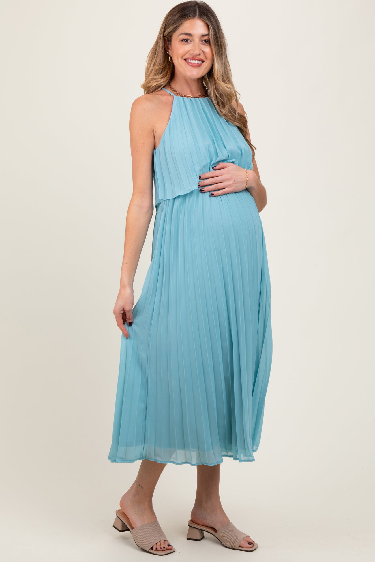 woman wearing a light blue pleated maternity dress and holding her baby bump