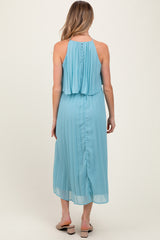 woman wearing a light blue pleated maternity dress with a flowing top and button detail at the back, showing her baby bump