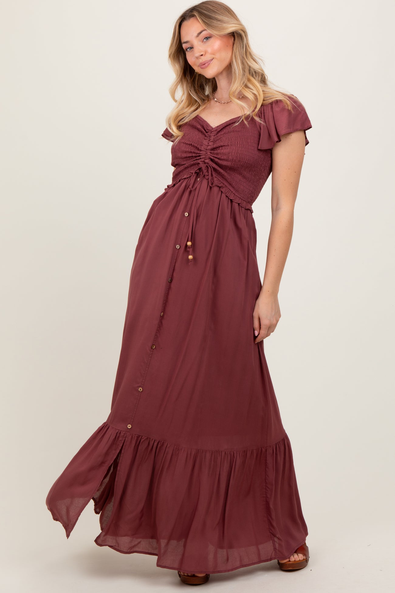 woman wearing a burgundy maxi dress with flutter sleeves and button details, posing gracefully