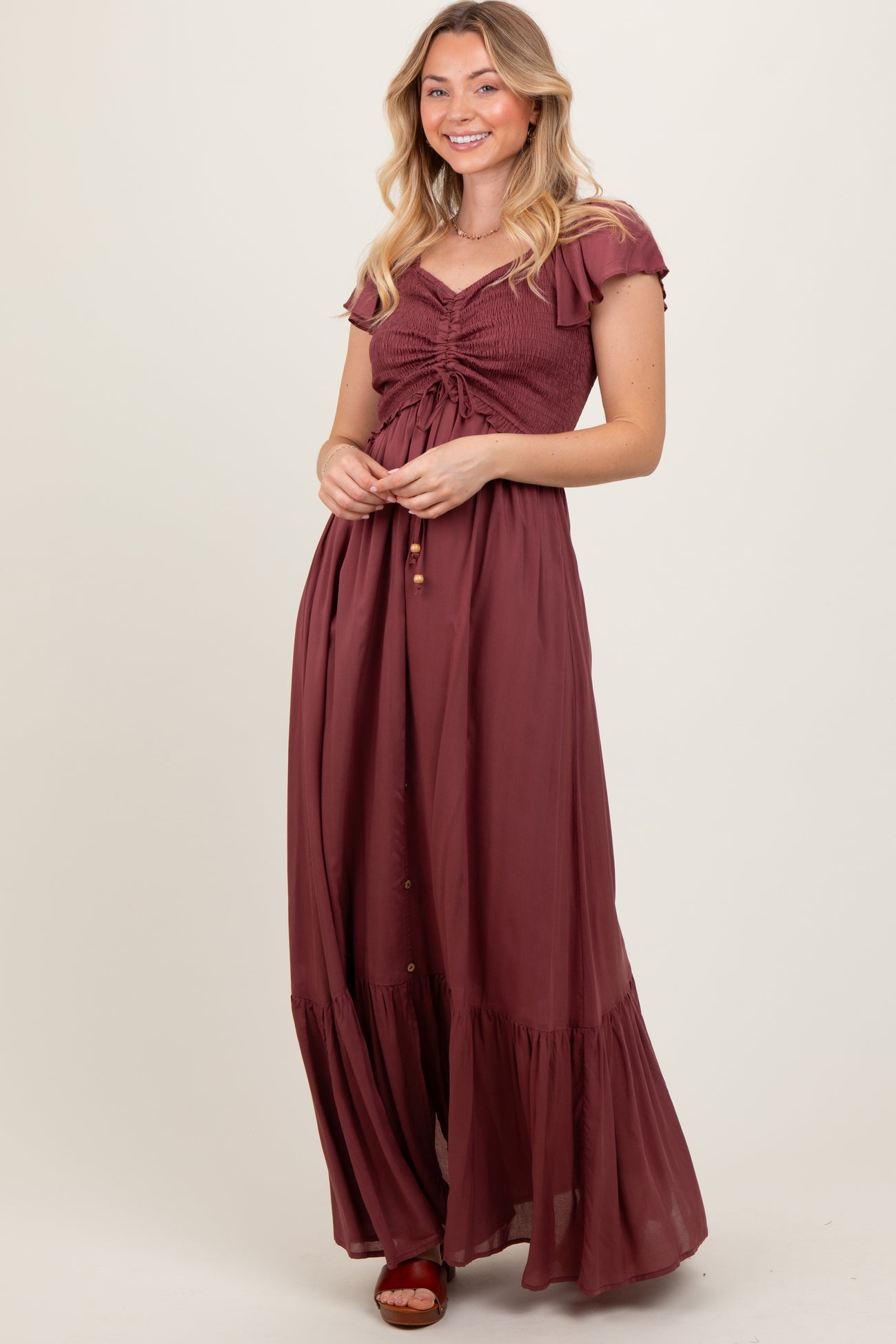 woman wearing a burgundy maxi dress with a smocked bodice and ruffle sleeves, styled with a button-down skirt and sandals