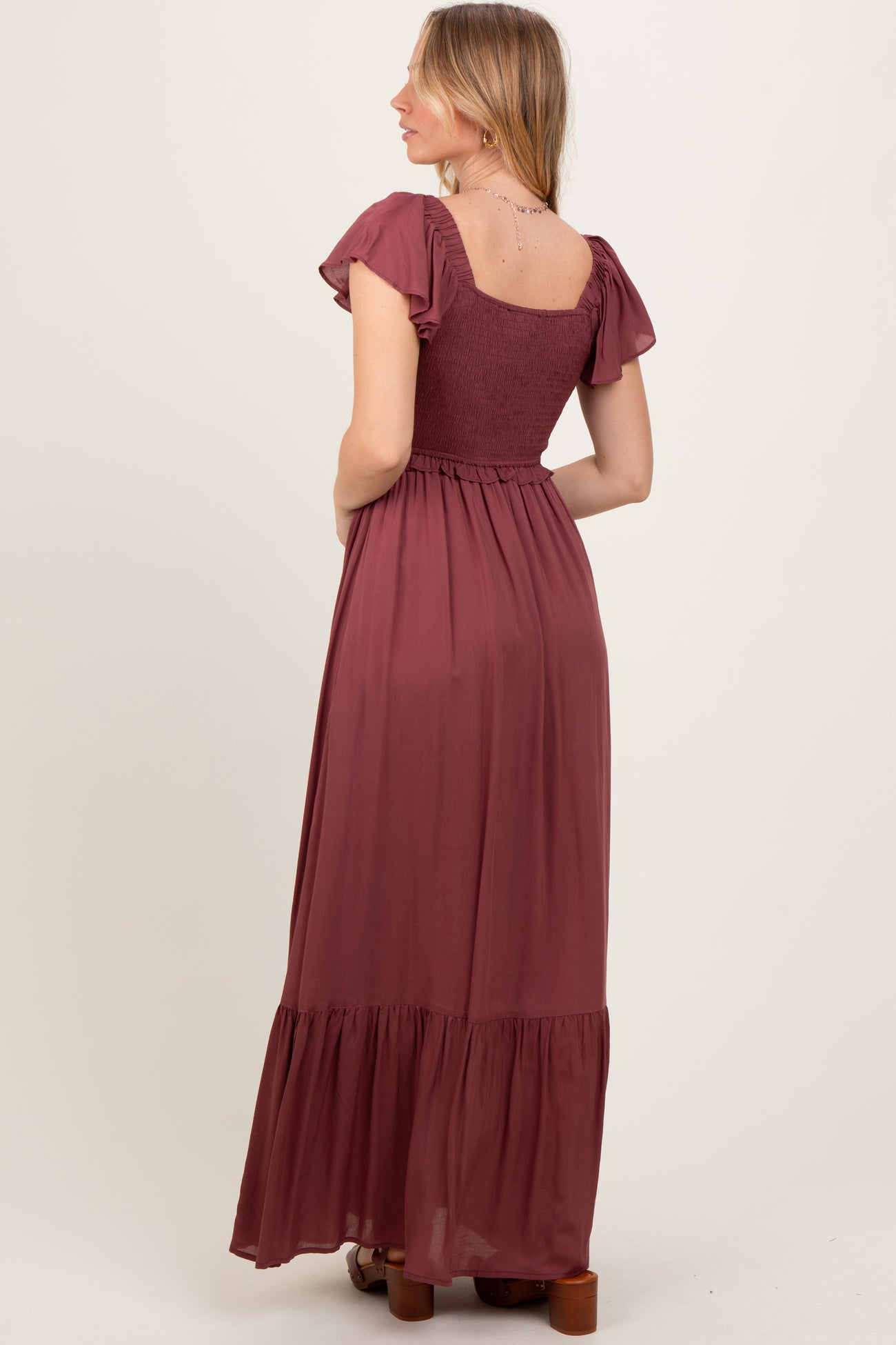 woman wearing a burgundy maxi dress with short ruffled sleeves and a smocked bodice, showing the back view