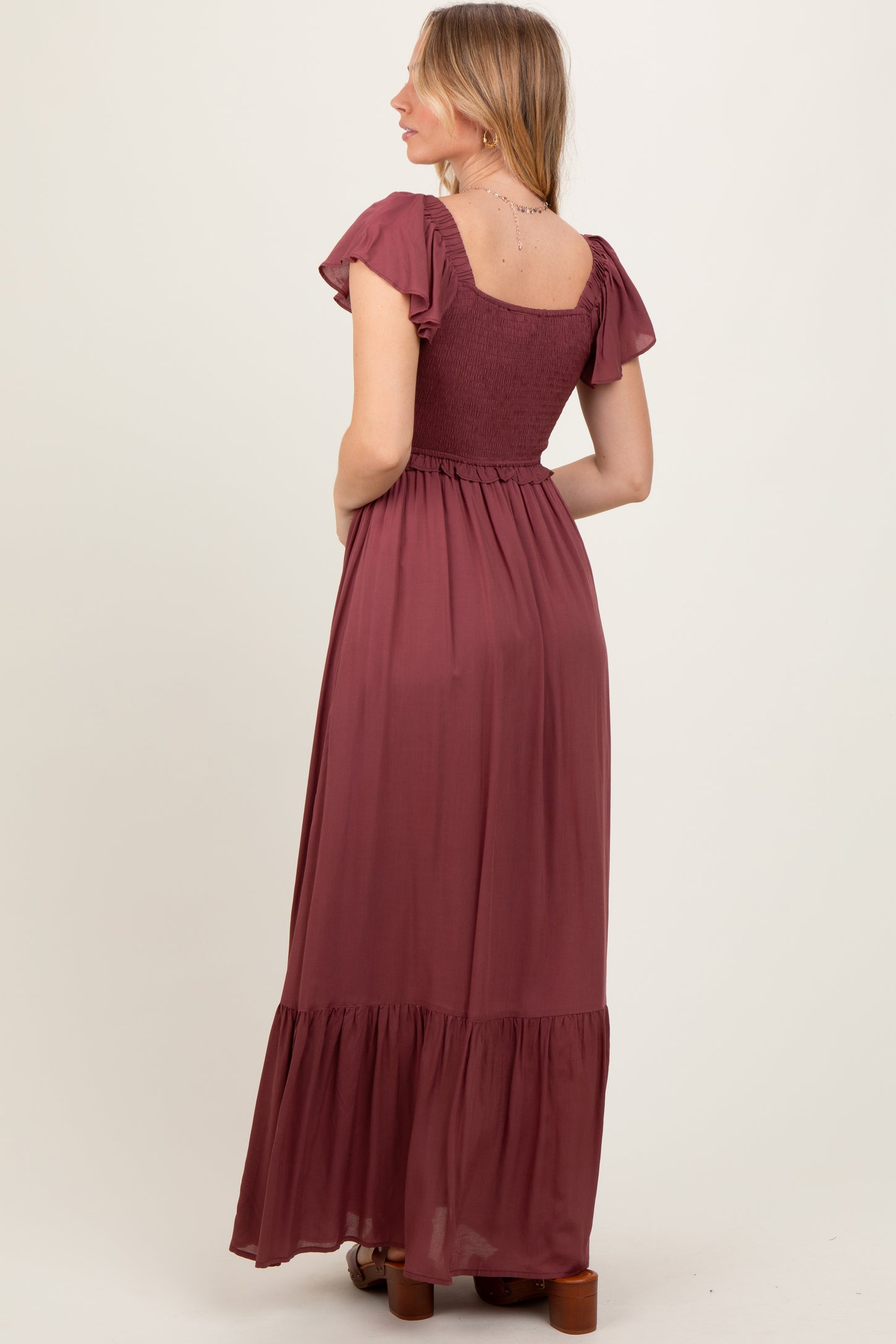 woman wearing a burgundy maxi dress with short ruffled sleeves and a smocked bodice, showing the back view
